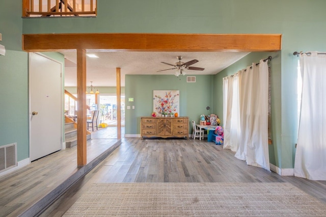 interior space featuring hardwood / wood-style floors, ceiling fan with notable chandelier, beamed ceiling, and a textured ceiling