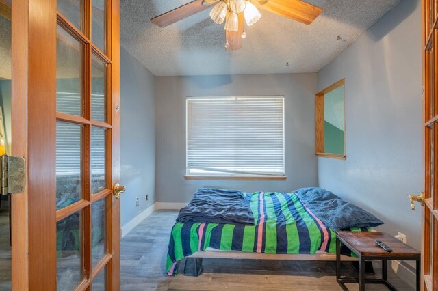 bedroom featuring hardwood / wood-style floors, french doors, ceiling fan, a textured ceiling, and multiple windows