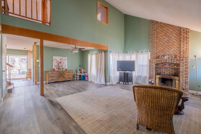 living room with ceiling fan, a brick fireplace, a towering ceiling, a textured ceiling, and light wood-type flooring