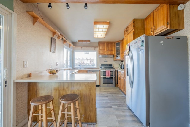 kitchen featuring a kitchen breakfast bar, light wood-type flooring, kitchen peninsula, and stainless steel appliances