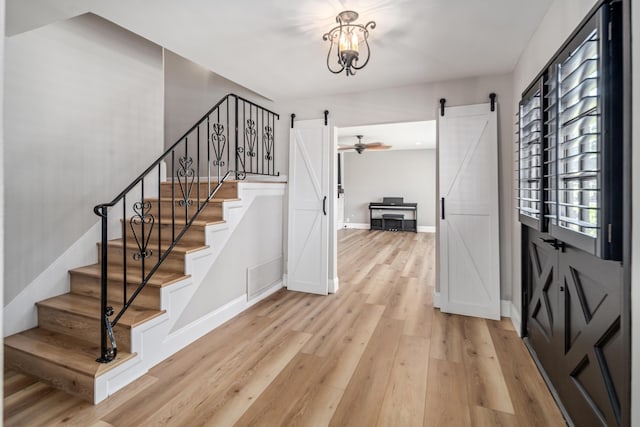 foyer entrance with a barn door, light hardwood / wood-style floors, and a notable chandelier