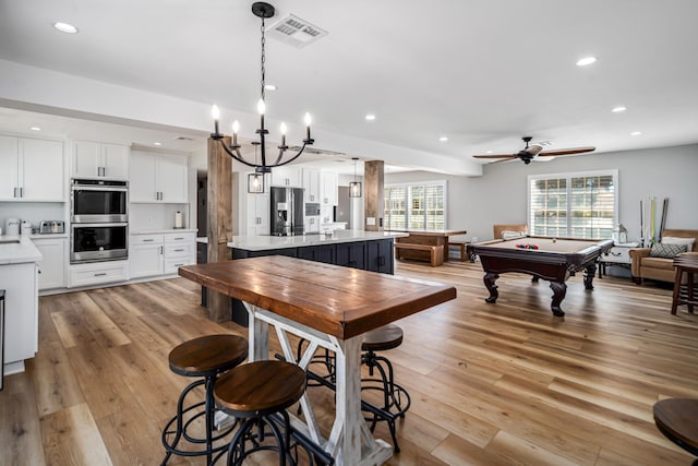 kitchen with ceiling fan with notable chandelier, stainless steel appliances, pendant lighting, light hardwood / wood-style flooring, and white cabinets