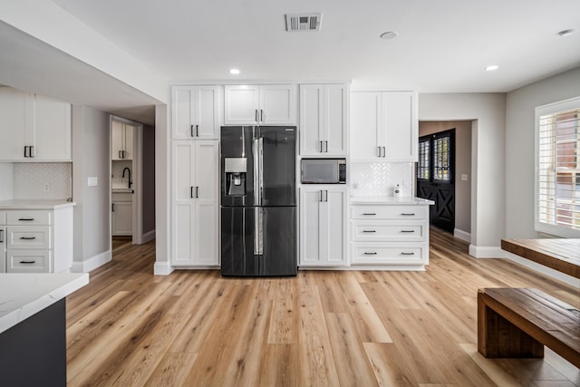 kitchen featuring refrigerator with ice dispenser, decorative backsplash, white cabinetry, and built in microwave