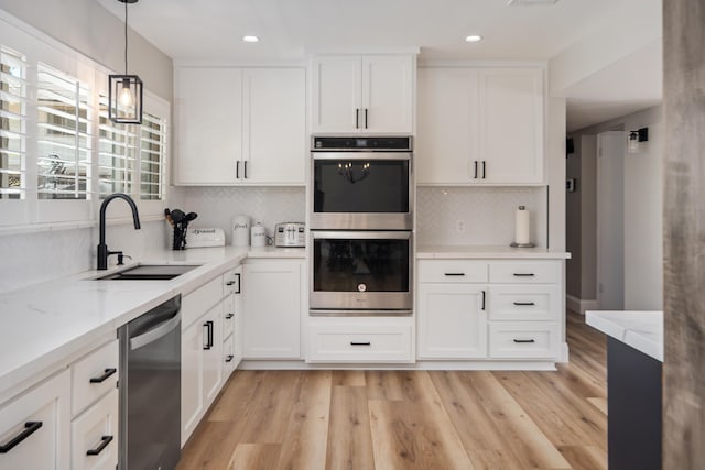 kitchen featuring white cabinetry, sink, stainless steel appliances, pendant lighting, and light wood-type flooring