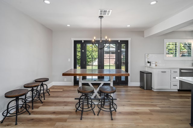 dining space featuring french doors, light wood-type flooring, and a notable chandelier