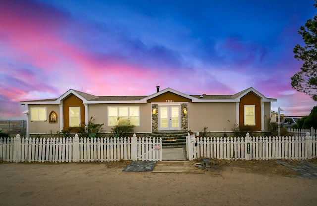 manufactured / mobile home with stucco siding, french doors, stone siding, and a fenced front yard