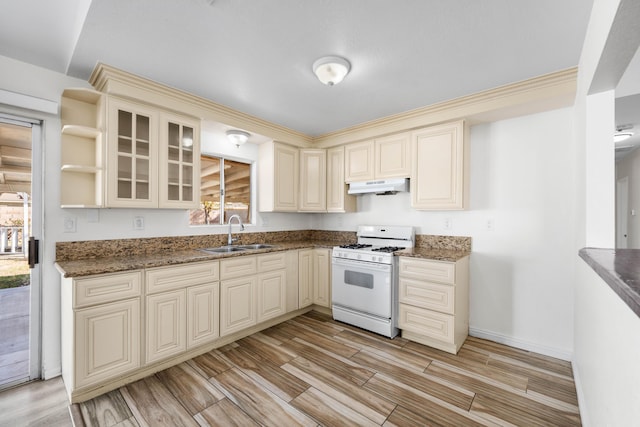 kitchen with dark stone countertops, sink, white gas range oven, and cream cabinets