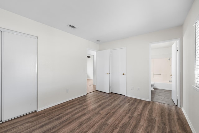 unfurnished bedroom with connected bathroom and dark wood-type flooring