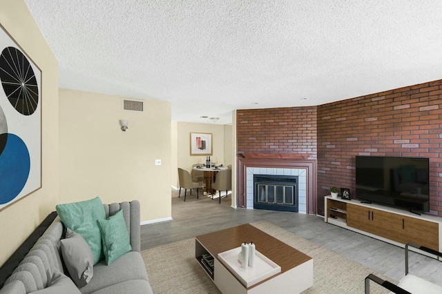 living room featuring a tile fireplace, a textured ceiling, and light hardwood / wood-style floors