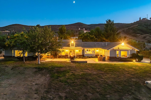 back house at dusk with a lawn, a mountain view, and a patio area