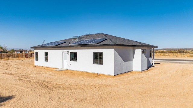 back of property with stucco siding, fence, and roof mounted solar panels