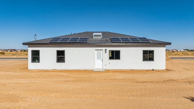 rear view of house with roof with shingles, stucco siding, and roof mounted solar panels