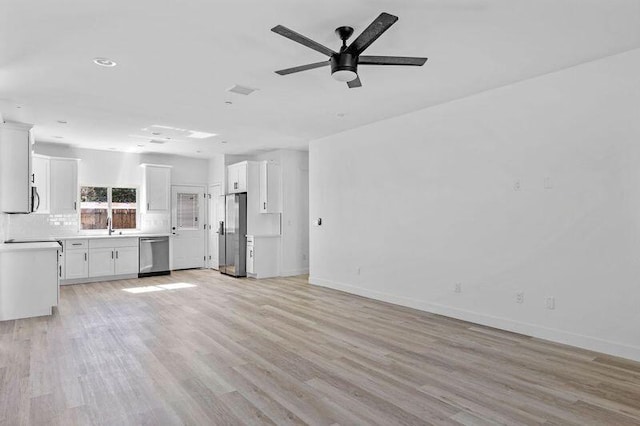 unfurnished living room featuring light wood-style floors, a sink, baseboards, and a ceiling fan