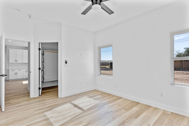 unfurnished bedroom with a walk in closet, light wood finished floors, a closet, ceiling fan, and baseboards