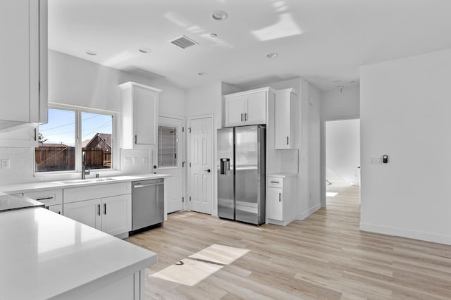 kitchen featuring light wood finished floors, stainless steel appliances, visible vents, decorative backsplash, and a sink