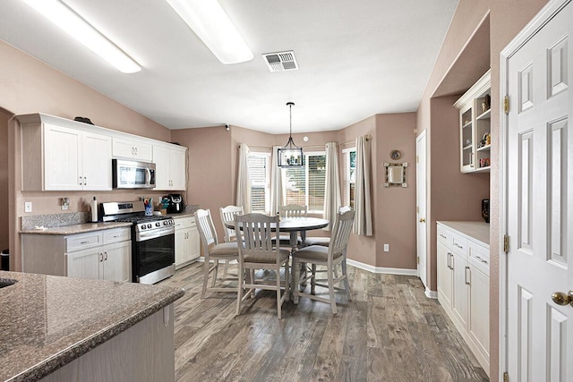 kitchen with light wood-type flooring, stainless steel appliances, decorative light fixtures, dark stone countertops, and white cabinetry