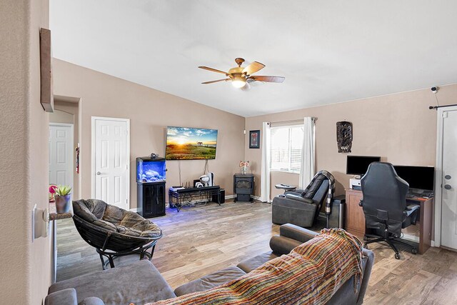 living room with vaulted ceiling, light hardwood / wood-style flooring, a wood stove, and ceiling fan