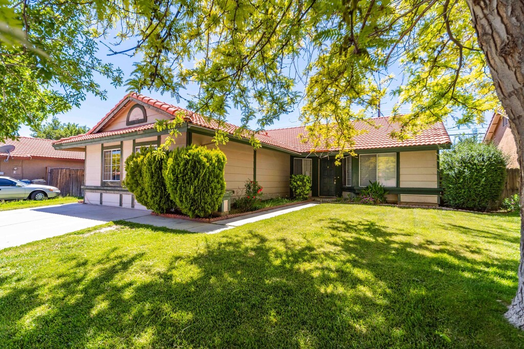 ranch-style home with a tiled roof, fence, and a front lawn