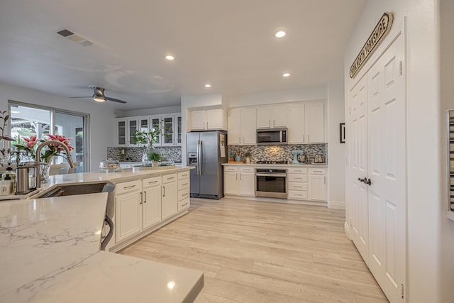 kitchen featuring decorative backsplash, appliances with stainless steel finishes, light stone counters, ceiling fan, and white cabinets