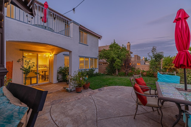 patio terrace at dusk featuring a balcony and a yard