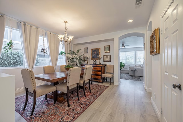 dining space with ceiling fan with notable chandelier and light wood-type flooring