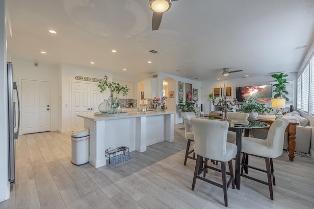 kitchen with a kitchen breakfast bar, ceiling fan, stainless steel fridge, light wood-type flooring, and kitchen peninsula