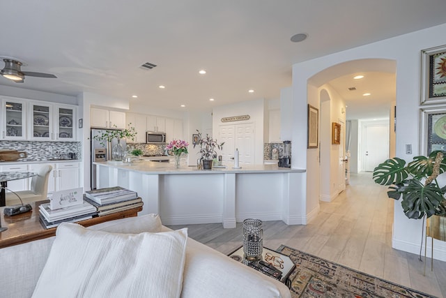 kitchen with ceiling fan, stainless steel appliances, kitchen peninsula, white cabinets, and light wood-type flooring