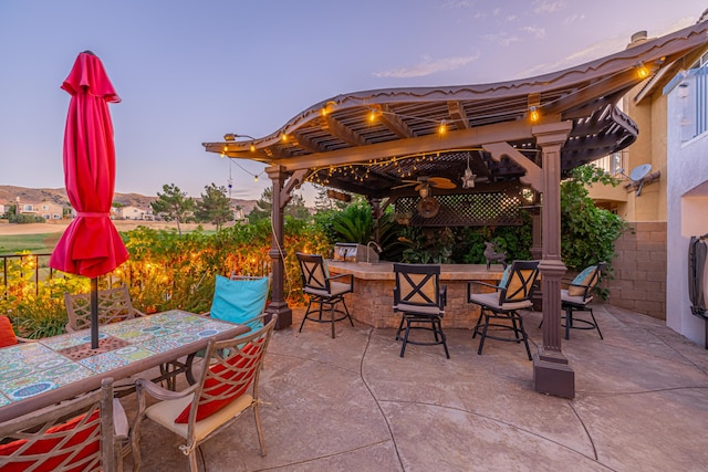 patio terrace at dusk with a pergola, ceiling fan, and an outdoor bar