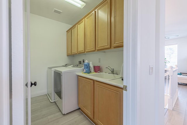 laundry room with cabinets, sink, washer and dryer, and light wood-type flooring