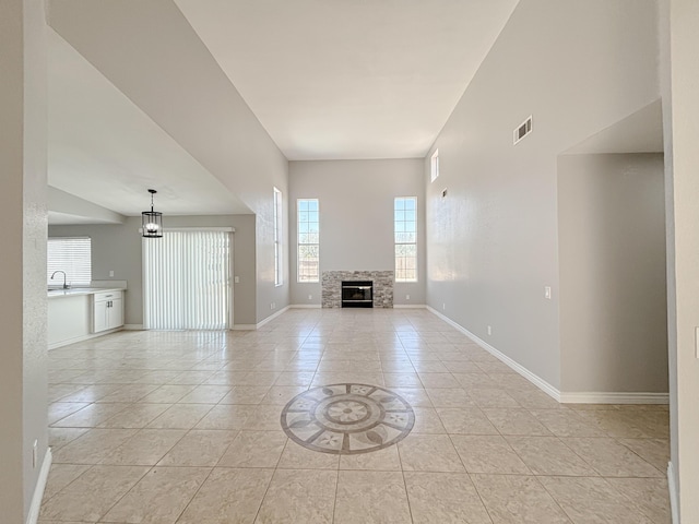 unfurnished living room featuring a chandelier, sink, a stone fireplace, and light tile patterned flooring