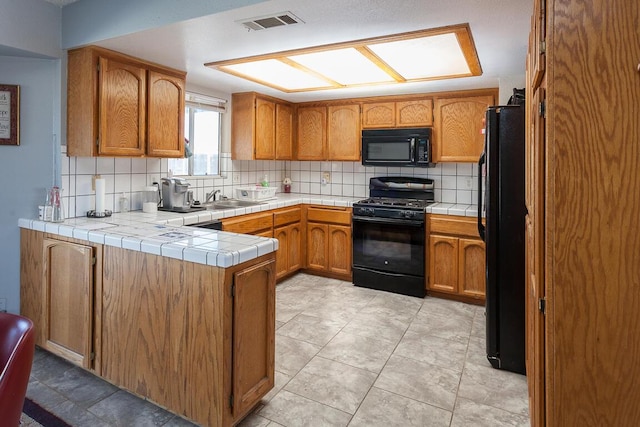 kitchen featuring tile countertops, black appliances, decorative backsplash, kitchen peninsula, and sink