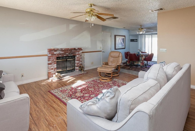 living room featuring a textured ceiling, ceiling fan, a fireplace, and light hardwood / wood-style flooring