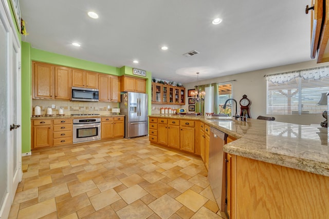 kitchen featuring pendant lighting, appliances with stainless steel finishes, sink, a notable chandelier, and light stone counters