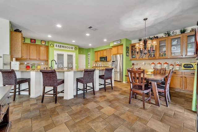 kitchen featuring kitchen peninsula, appliances with stainless steel finishes, decorative light fixtures, light stone counters, and a kitchen bar