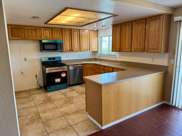 kitchen with visible vents, appliances with stainless steel finishes, brown cabinetry, a sink, and a peninsula