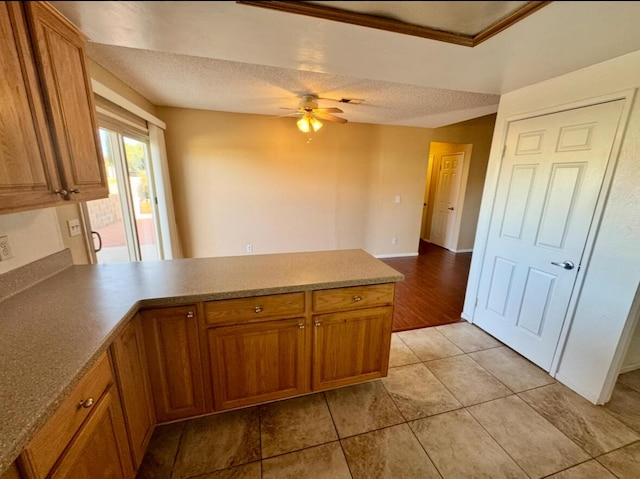 kitchen featuring a peninsula, a ceiling fan, brown cabinets, and a textured ceiling