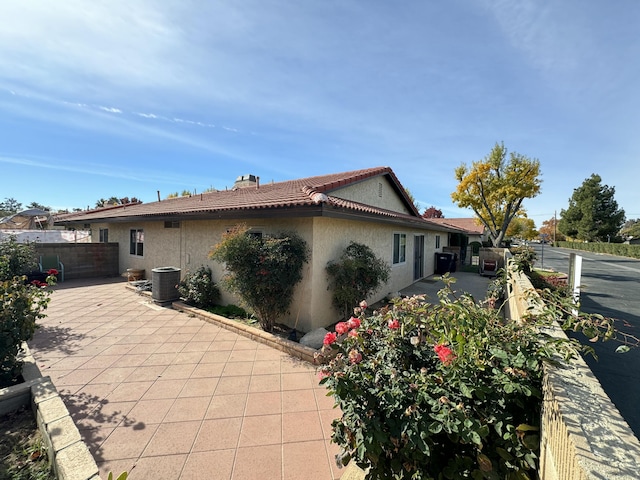 view of home's exterior with a chimney, stucco siding, central AC unit, a patio area, and fence