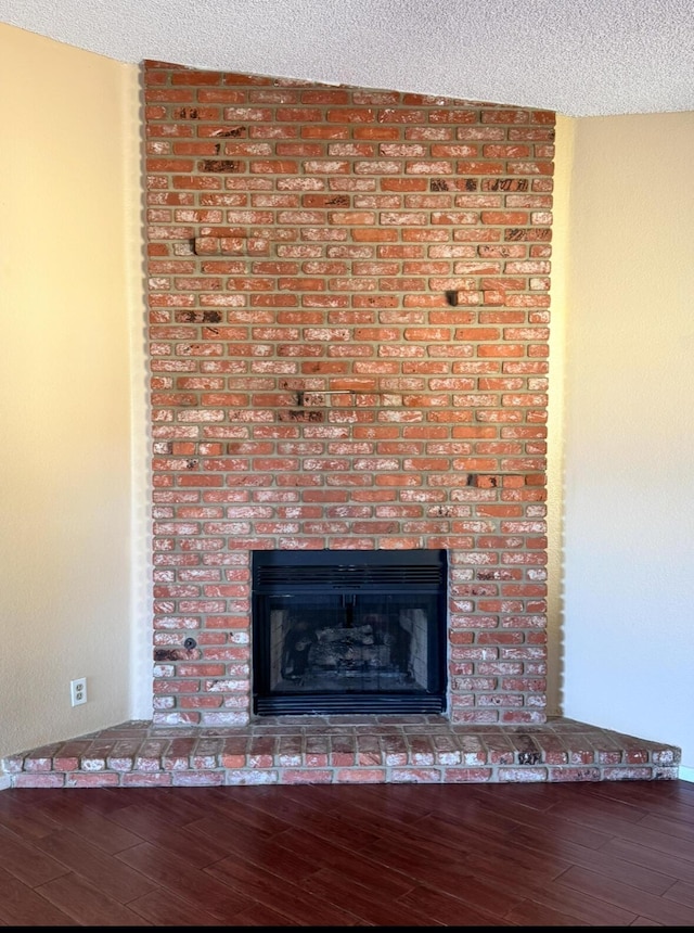 interior details with a brick fireplace, a textured ceiling, and wood finished floors