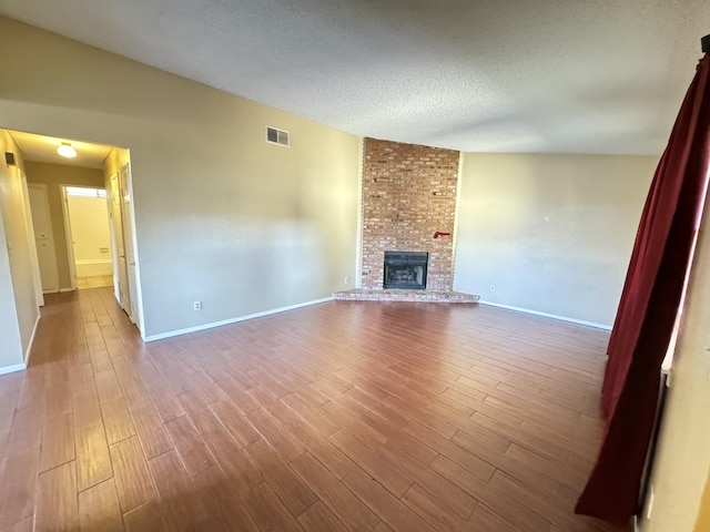 unfurnished living room with dark wood finished floors, a fireplace, visible vents, a textured ceiling, and baseboards