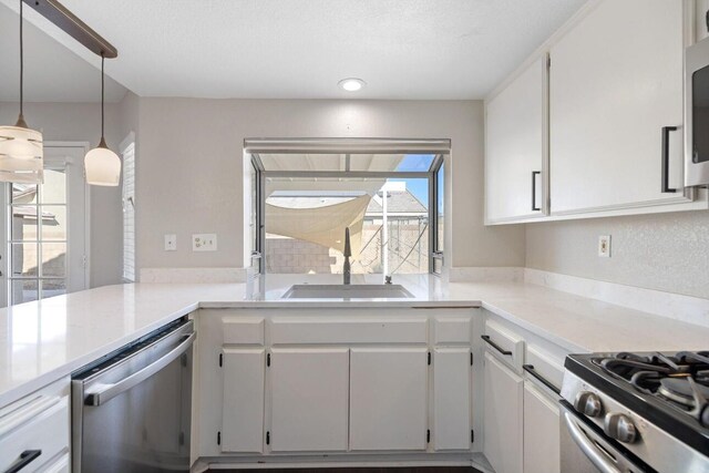 kitchen featuring sink, hanging light fixtures, kitchen peninsula, white cabinets, and appliances with stainless steel finishes