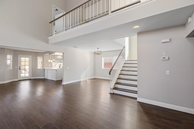 unfurnished living room with dark hardwood / wood-style flooring, a towering ceiling, and an inviting chandelier