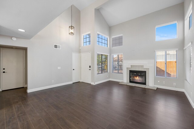 unfurnished living room featuring a tiled fireplace, a towering ceiling, dark wood-type flooring, and an inviting chandelier