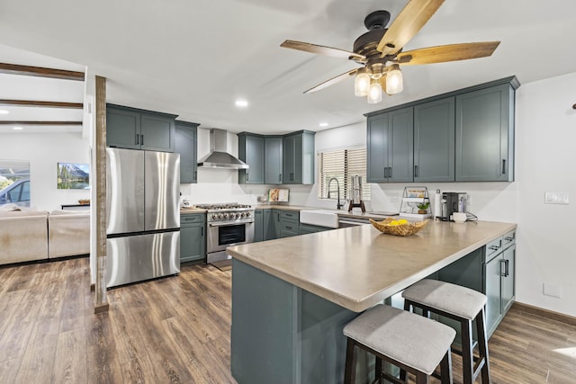 kitchen with a kitchen breakfast bar, a sink, a peninsula, stainless steel appliances, and wall chimney exhaust hood