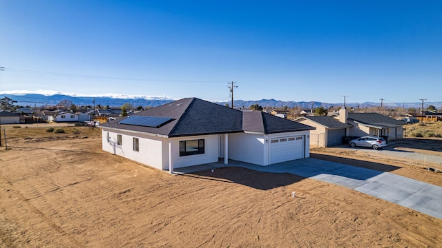 ranch-style house with a garage, stucco siding, solar panels, a mountain view, and driveway