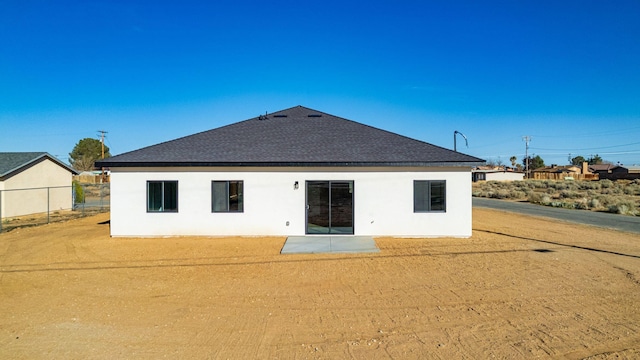 rear view of property with roof with shingles, a patio, stucco siding, and fence