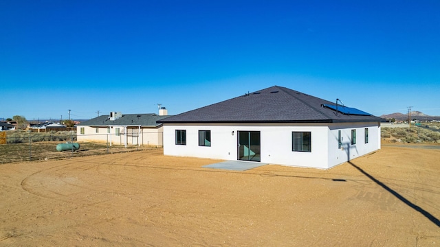 back of property featuring roof with shingles, solar panels, fence, and stucco siding