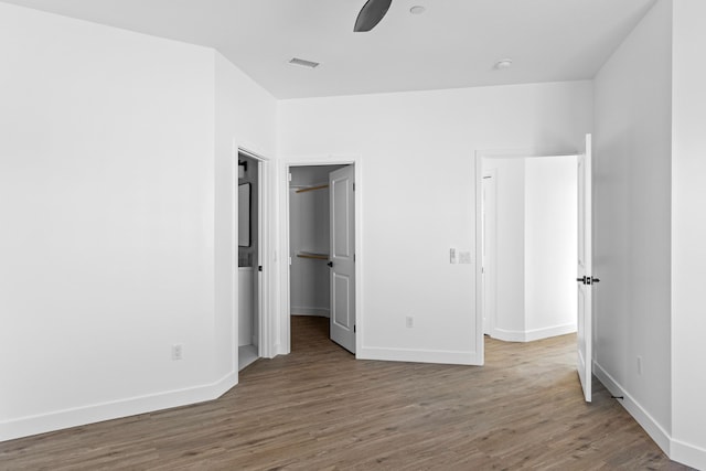 unfurnished bedroom with a walk in closet, visible vents, baseboards, and wood finished floors