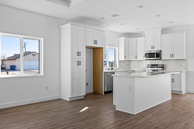 kitchen featuring dark wood-type flooring, white cabinets, visible vents, stainless steel appliances, and backsplash