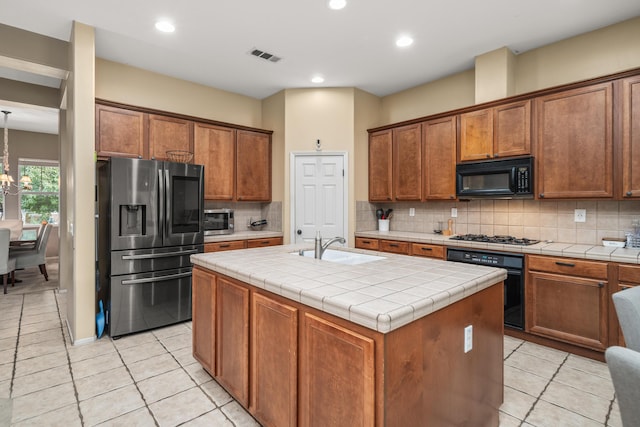 kitchen with a kitchen island with sink, black appliances, an inviting chandelier, tile counters, and light tile patterned flooring