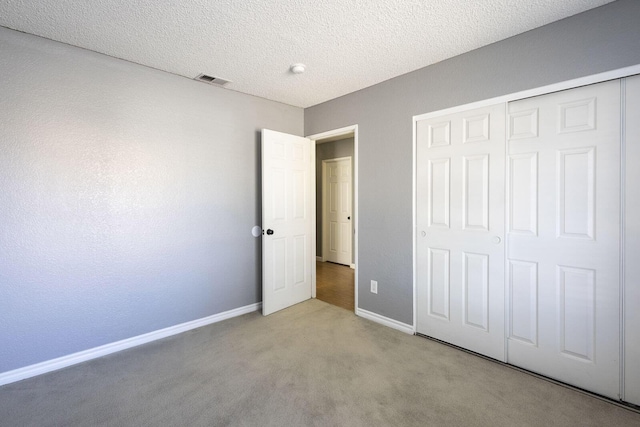 unfurnished bedroom with a textured ceiling, visible vents, carpet floors, baseboards, and a closet